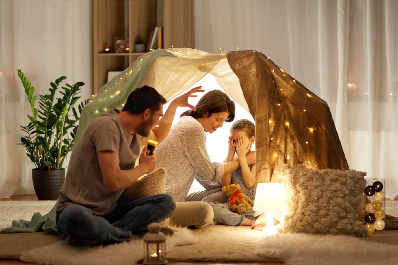 A family enjoys a spooky story in a homemade fort in their living room