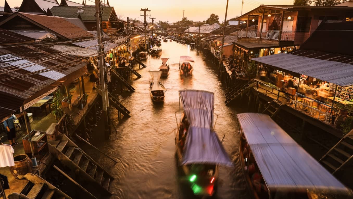 Ships pass along a busy, well-lit urban canal at sunset