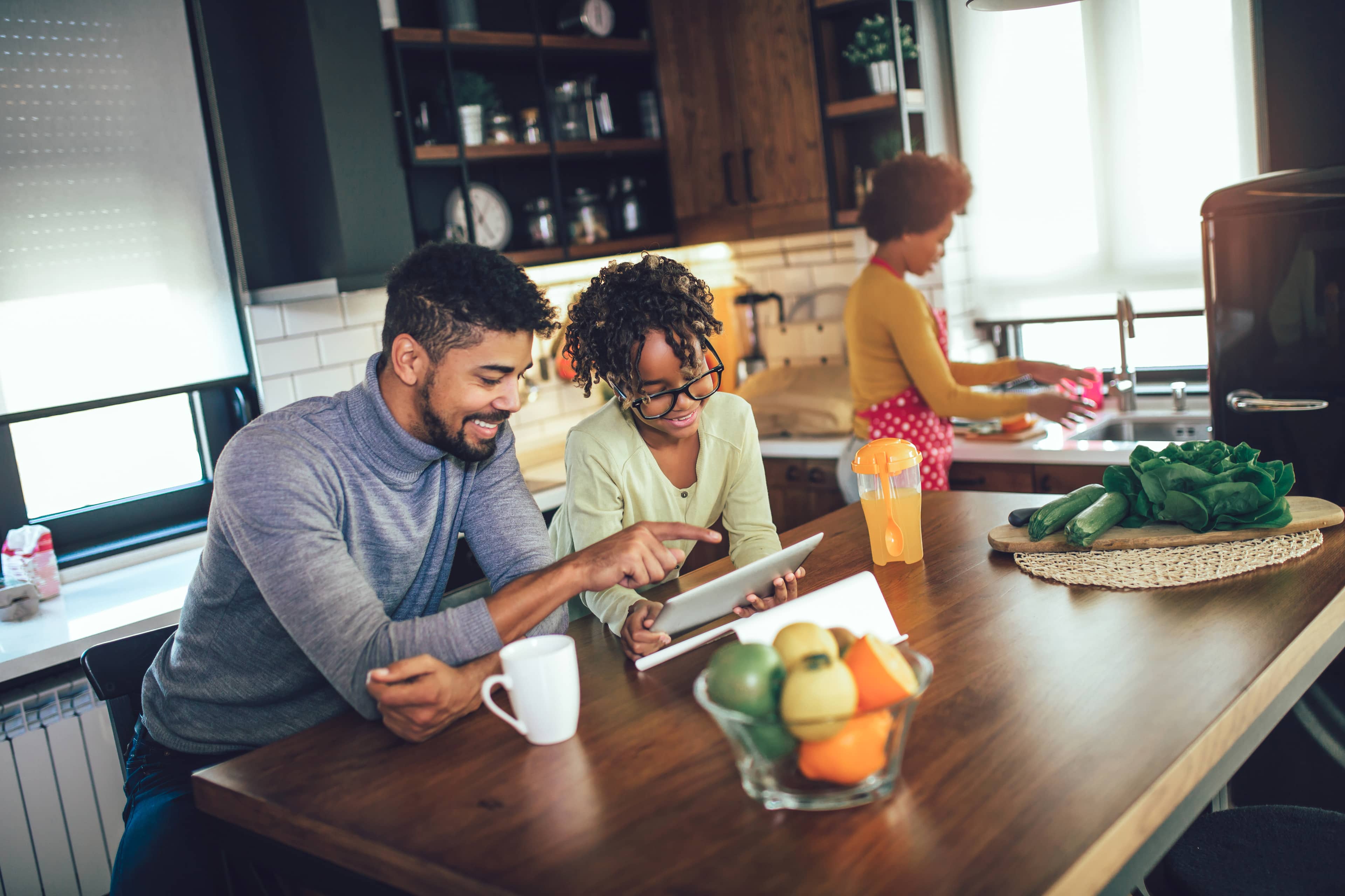 A young Black family enjoys some audio entertainment on a tablet in a kitchen