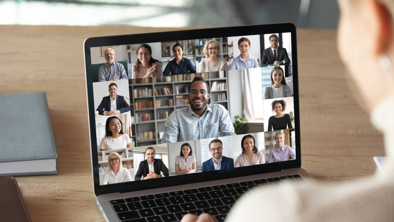 A woman engages in a conference call on a laptop with many other individuals